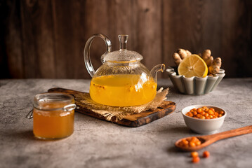 Teapot with sea buckthorn tea. A warming winter drink. Vitamin tea. Sea buckthorn tea with honey, lemon and ginger on a gray background.