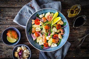 Salmon salad - smoked salmon, white smoked cheese and fresh vegetables on wooden table
