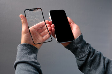 male hand close-up holds mobile phone with a cracked protective glass screen, broken phone glass,...