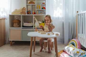 A little girl playing with wooden blocks on the table in playroom.  Educational game for baby and...