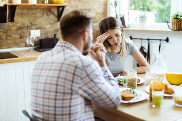 Young woman having a headache while arguing with her boyfriend during breakfast time at home
