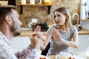 Young angry woman having relationship difficulties with her boyfriend during breakfast time in dining room
