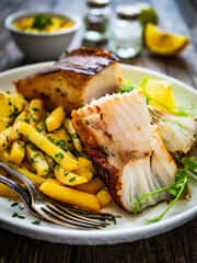 Fish dish - fried halibut with French fries and lemon on wooden table
