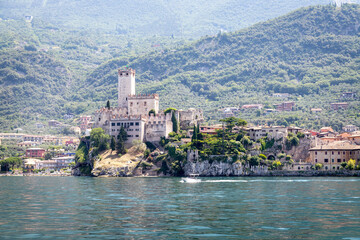 Fototapeta na wymiar Idyllic coastline scenery in Italy, captured from the water. Blue water and a cute village at lago di garda, Malcesine