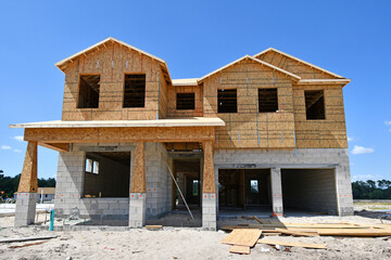Incomplete new two story residential home under construction at wood frame under blue skies in...