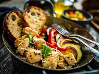 Fried chicken nuggets with bread and vegetables in frying pan on wooden table
