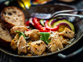 Fried chicken nuggets with bread and vegetables in frying pan on wooden table
