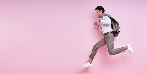 Fototapeta na wymiar Excited man in shirt and tie carrying jacket on shoulder while jumping against pink background