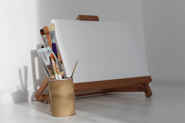 Empty copy space canwas on wood easel and paintbrush in artistic workshop interior