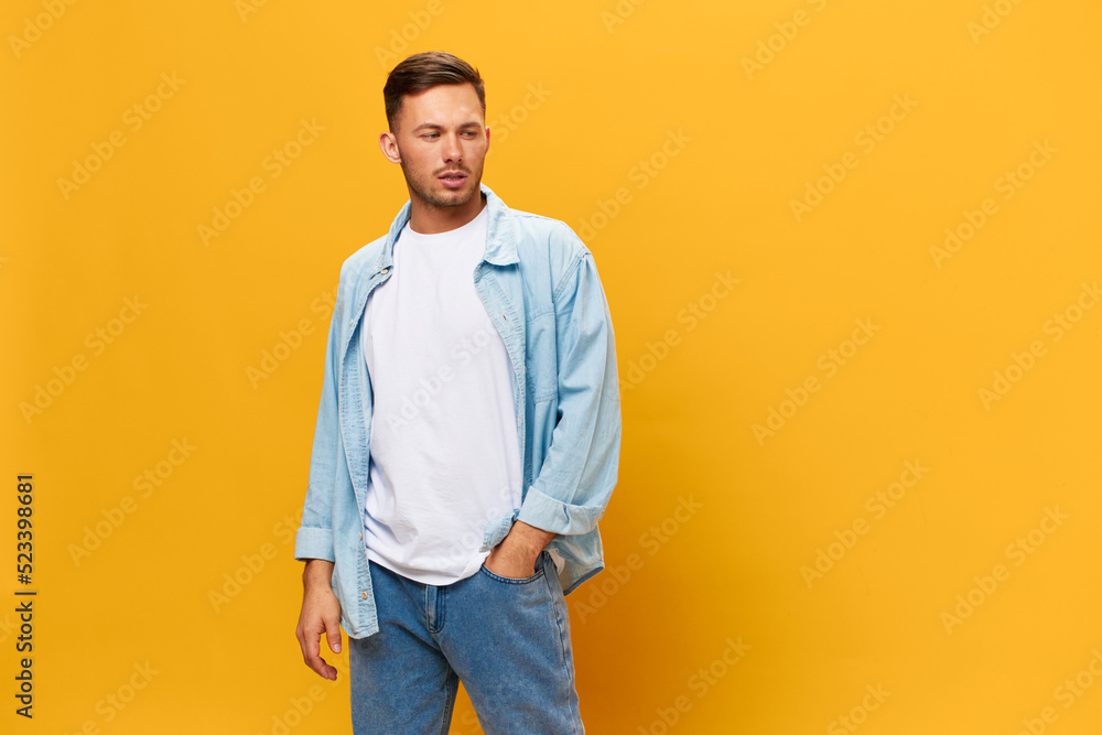 Wall mural Pensive thoughtful tanned handsome man in blue basic t-shirt hold hands on pocket look aside posing isolated on yellow studio background. Copy space Banner Mockup. People emotions Lifestyle concept