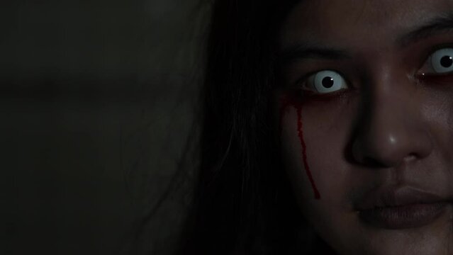 Ghost of woman in halloween concept. Close up horror face of woman with blood fade drop from eyes in the dark background nightmare screaming on hell is monster girl or female dead characters at night.