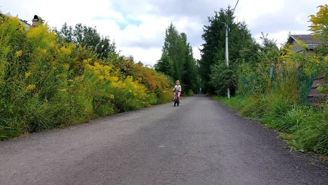 A little girl rides a bike on a rural road. The moment of summer lifestyle of a happy childhood.