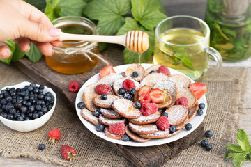 mini pancakes chocolate pancakes with blueberries and raspberries on a white plate A man pours honey on pancakes On a wooden background