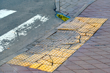 Cracked yellow tactile tiles on asphalt road in front of pedestrian crossing. Damaged warning tiles...