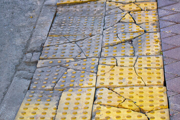 Damaged and dirty yellow tactile tiles on asphalt road. Damaged warning tiles for blind peoples on...