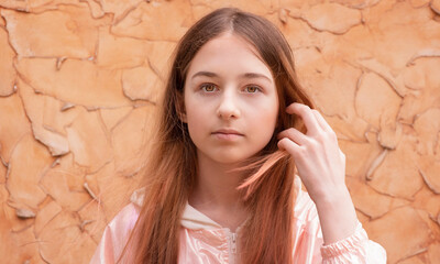 Girl teenager portrait at beige wall. The girl fixes her hair.