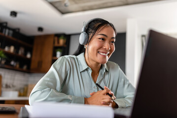 Young Asian women attending online foreign language classes. Sitting in front of a laptop computer with headphones listening to courses and taking notes.