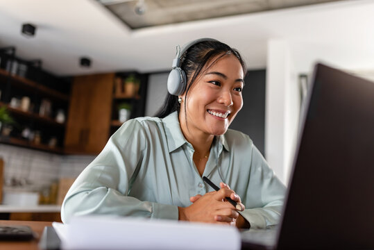 Young Asian women attending online foreign language classes. Sitting in front of a laptop computer with headphones listening to courses and taking notes.