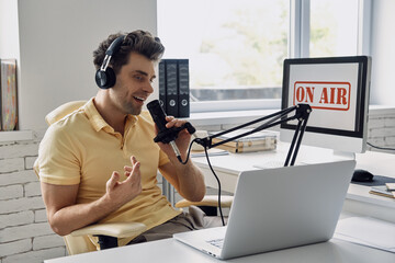 Handsome young man using microphone and gesturing while recording podcast in studio
