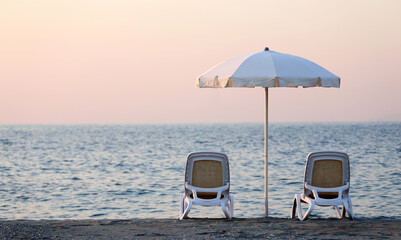 Beach chairs with umbrella and sand beach in summer sunset. Italy. Summer vacation travel concept.