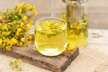 St. John's wort tea is a therapeutic healthy drink A teapot and a cup on a wooden background A bouquet of St. John's wort on the table The concept of medicinal herbs, phytotherapy