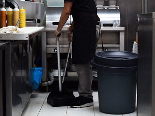 Restaurant kitchen employee sweeping the floor