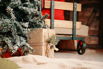 Christmas tree in snow, gift boxes, warm blanket, wooden trolley with pillows and decorations in New Year's interior of photo studio. Festive atmosphere.
