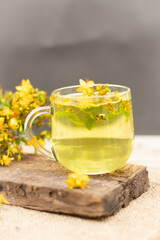 St. John's wort tea is a therapeutic healthy drink A cup on a wooden background A bouquet of St. John's wort on the table The concept of medicinal herbs, phytotherapy Vertical photo