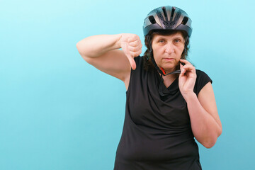 An upset woman wearing a bicycle helmet shows his thumb down on a blue background. Insurance. Injury. Protect. Secure. Protective. Perfect. Cycle. Express. Accident. Guard. Hobbies. Tool. Protector