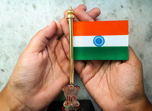 Miniature Indian National Flag on a metal stand with national emblem 'Ashok Stambh' in a hand  on white marble background to show respect, love, care and protection concept for the country.