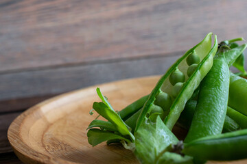 a pile of open green pea pods on a wooden plate, soft focus.
