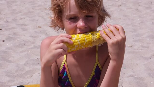Teenage girl on the beach in a bathing suit. The child enjoys eating corn in the sun. nice summer picture