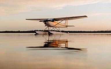 A seaplane float plane floats on a lake at sunset with soft lighting, the aircraft reflects in the...