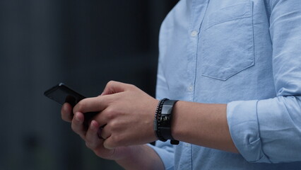 Businessman using smartphone texting outdoors. Male hands hold device closeup.