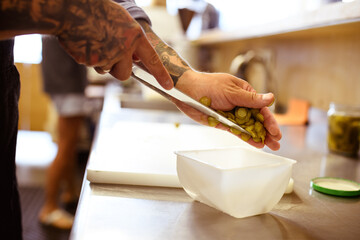 Obraz premium Partial shot of tattooed chef holding cut pickled cucumbers in kitchen 