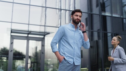 Handsome man speaking cellphone at glass office building. Modern corporate area