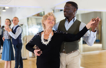 Elderly woman learning ballroom dancing in pair in dance studio