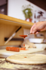 Faceless shot of chef pouring red sauce on pizza dough in cafe kitchen 