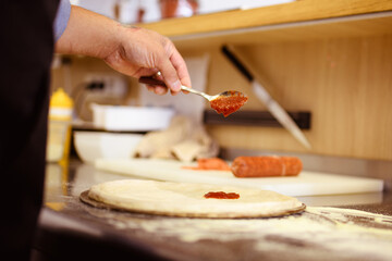 Faceless view of cook pouring red sauce on pizza dough near flour on cafe kitchen 