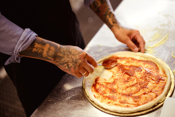 Faceless shot of tattooed chef pouring sauce on raw pizza in kitchen 