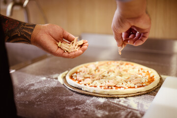 Partial view of tattooed chef putting meat on raw pizza near flour on cafe kitchen 