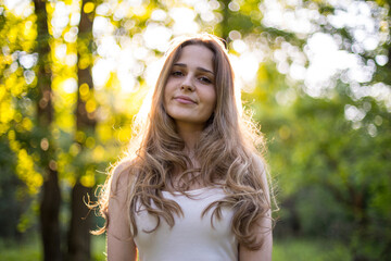 Beautiful young Russian girl dressed in a white dress, walks through the forest among the oaks in the rays of the sunset