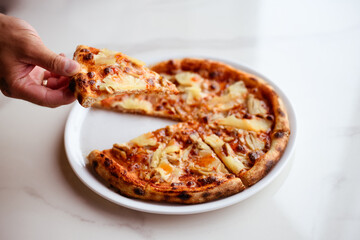 Faceless view of man holding piece of delicious pineapple pizza on marble background 