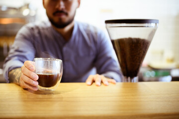Partial shot of blurred barista holding glass of coffee in coffee shop 
