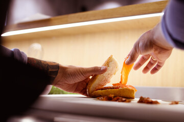 Faceless shot of tattooed chef putting salmon on ciabatta near sundried tomatoes in cafe kitchen 