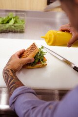 Partial view of tattooed chef holding olive oil while making sandwich with salmon in cafe kitchen 