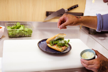 Partial view of chef pouring cheese on fresh ciabatta with salmon in cafe 