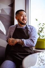 Smiling asian small business owner in apron looking away in cafe 