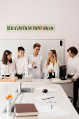 School chemistry teacher shows children flasks with liquids for experiments in the laboratory. Education concept. Group lesson of classmates at chemistry lesson.