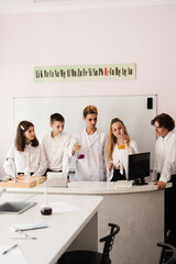School chemistry teacher shows children flasks with liquids for experiments in the laboratory. Education concept. Group lesson of classmates at chemistry lesson.